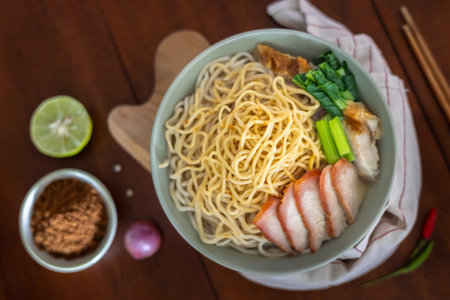A close-up of Braised noodle soup with roasted red pork in a bowl served on a wooden plate with seasoning and chopsticks. Top view. Flat lay.の写真素材