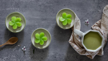 Top view of a steamed pandan layer cake on small cups, served with a cup of green tea, a traditional...