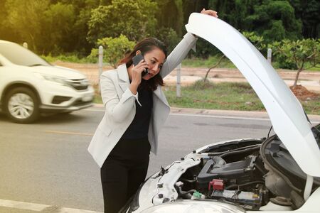 Woman business calling phone fore help from the broken car. Woman business at broken car on road and calling on cellphone for help.の写真素材