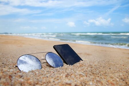 Sunglasses and phone are placed on beach and reflections of bright sky.Summer holiday on the beach concept.の写真素材