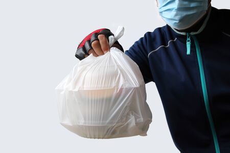 Food service providers wear masks. Sending plastic bags with food to customers who order food online isolated on white background.Ordering food online Was very popular during the period of the Covid-19 virus in Southeast Asia.の写真素材