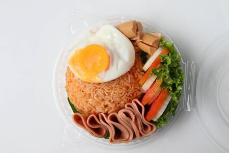 Fried rice with fried egg, bacon and vegetables In a round plastic box isolated on white backgroundの写真素材