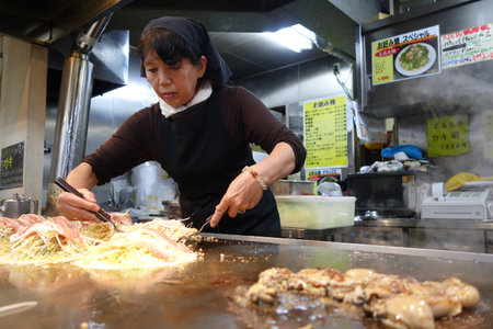HIROSHIMA, JAPAN - DECEMBER 10: Japanese cook prepares the famous okonomiyaki for the guests in Hiroshima, Japan on December 10, 2014. Hiroshima okonomiyaki is a must try food in Hiroshima, Japan.のeditorial素材