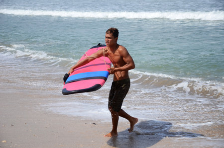 Bali, Indonesia- 18 Oct, 2019: Happy surfer with surfboard along the sea shore going into the seaのeditorial素材