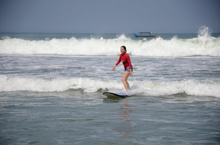 Bali, Indonesia- 18 Oct, 2019: Young surfer ride on surfboard with fun on sea waves in Bali island,...