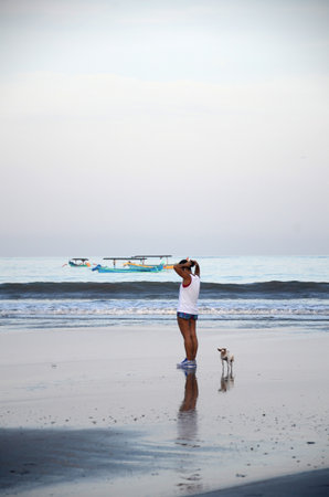 Bali, Indonesia- 18 Oct, 2019: Woman with dogs walking at tropical beach in the morning in Bali, Indonesiaのeditorial素材