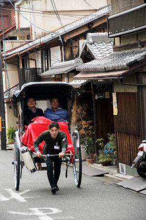 Kyoto, Japan- 27 Nov, 2019: Jinrikisha driven by an unidentified driver carrying two tourists in Kyoto.The word jinrikisha is of Japanese origin and means human-powered vehicle.のeditorial素材