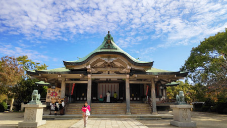 Osaka, Japan- 01 Dec, 2019: Closeup entrance and front of Hokoku-jinja Japanese shrine with trees on bright blue sky background.のeditorial素材