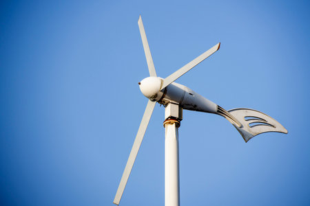 Small electricity generating wind turbine spinning against blue sky
