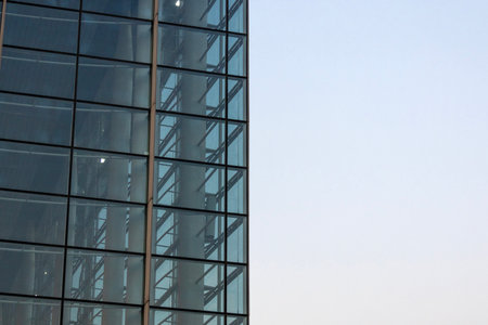 Office building stands tall against a clear blue sky, reflecting modern architecture and urban...