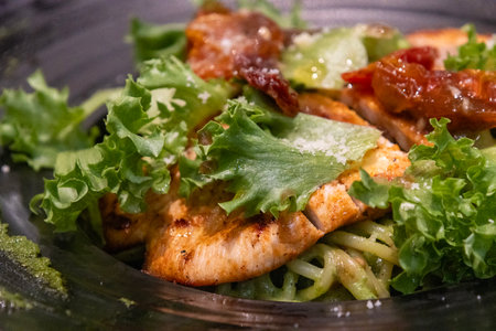 Pasta with grilled chicken and basil pesto sauce on a black plateの写真素材