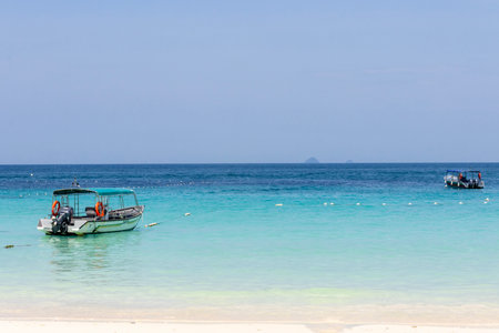 Small boat parks on the shore of Redang Island with crystal clear water with white sandの写真素材