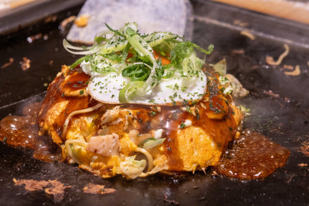 Okonomiyaki on a sizzling hot pan. Okonomiyaki is a savory Japanese pancake made from a flour batter...