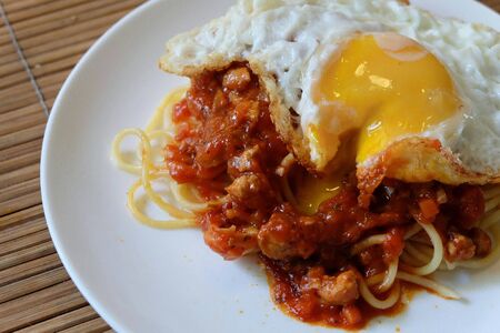 Spaghetti with red chicken tomato sauce topping with fried egg on white plateの写真素材