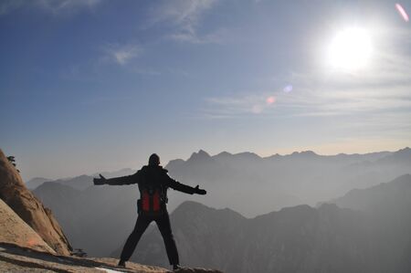 Arms opened saluting the sun on top of mountain