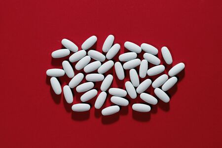 A bunch of white pills on the red backgroundの写真素材