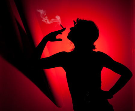 silhouette of woman smoking. Profile of woman pulling smoke on red backgroundの写真素材