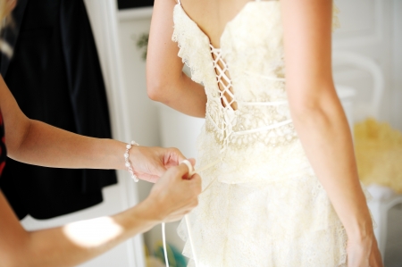 Bridesmaid hands helping the bride to dress for the wedding ceremonyの写真素材