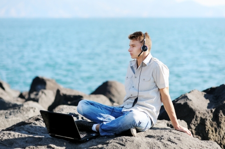 handsome boy listening to music from his laptop near the seaの写真素材