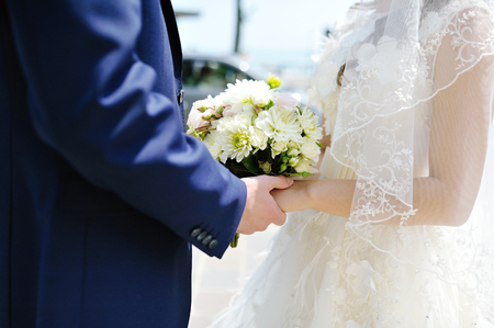 groom holding the bride's hand and beautiful white wedding bouquetの写真素材