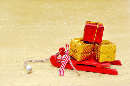 Christmas red sleigh and gift box decoration on golden backgroundの写真素材