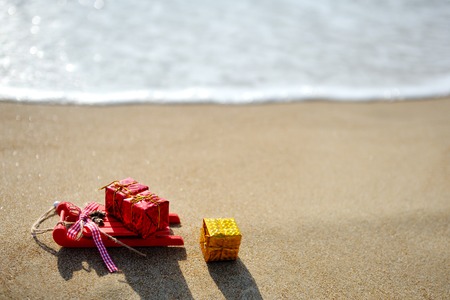 Christmas red sleigh and gift box decoration on sea beach backgroundの写真素材