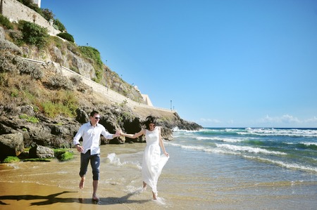 happy couple holding hands running on the beach near sea in wedding dayの写真素材