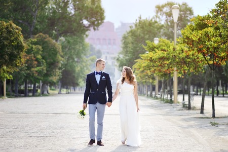 bride and groom walking in a park holding hands in wedding dayの写真素材