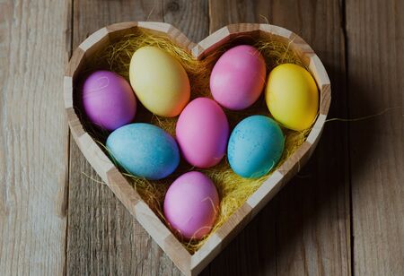 Colorful Easter eggs in a wooden heart shaped bowlの写真素材