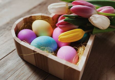 Heart shaped wooden bowl, colored eggs and tulips - happy Easterの写真素材