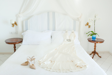 Bridal white dress and shoes on bed in wedding dayの写真素材