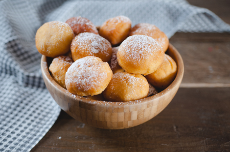 Homemade sweet dessert pastry balls covered with icing sugar in a wooden bowlの写真素材