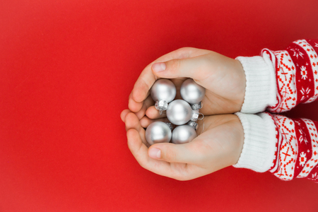 Child hands holding silver christmas baubles on red backgroundの写真素材