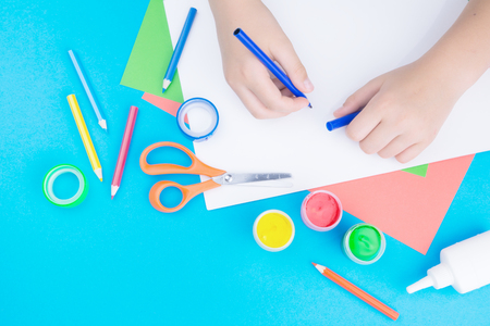 color paper, paint and hands of a child holding a marker pen on blue backgroundの写真素材