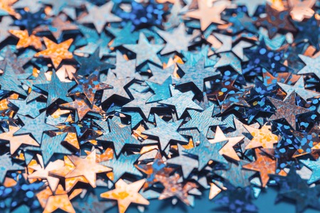 Blue and orange star shaped festive confetti background, close up with copy space