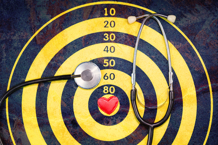Red heart in the center of dartboard with stethoscope and a double exposure crack, elderly health concept with copy space in flat layの写真素材