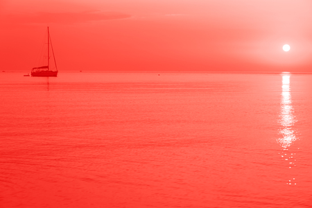Trendy living coral color of year 2019. Sailing boat with rising sunの写真素材