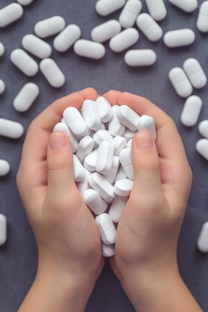 Two kids hands handful of white tablets, drugs and medicine safety and consumption concept with copy spaceの写真素材