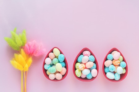 Happy Easter bright greeting card with small eggs in three egg shaped bowls, on pink background with copy space in flat layの写真素材