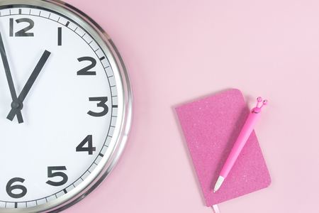 Part of analogue plain wall clock with trendy feminine pink notepad and a funny pen. Close up flat lay with copy space, time management with agenda concept and lunch timeの写真素材