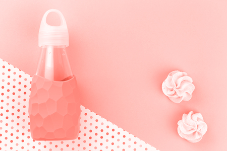 Monochrome trendy living coral color feminine glass water bottle with two cookies on a polka dotted background, flat lay with copy space for bloggerの写真素材