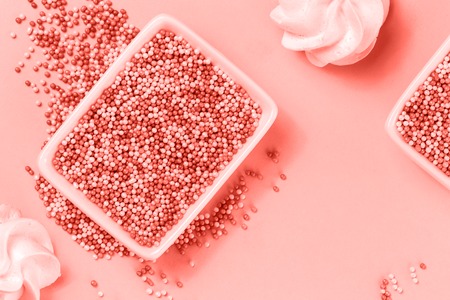 Shades of living coral nonpareils cake candy sprinkles in two white rectangular bowls and cookies in flat lay with copy space. Party celebration or bakery conceptの写真素材