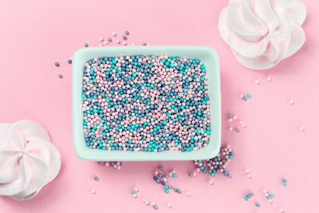 Colorful nonpareils cake candy sprinkles in two white rectangular bowls and cookies on pink background in flat lay with copy space. Party celebration or bakery conceptの写真素材