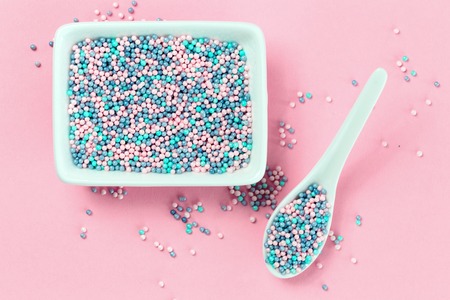 Colorful nonpareils cake candy sprinkles in two white rectangular bowls and spoon on pink background in flat lay with copy space. Party celebration or bakery conceptの写真素材