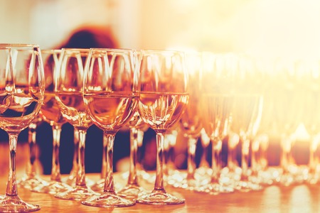 Row of white wine or sparkling glasses at the bar counter blurring away with light flare at sunset...