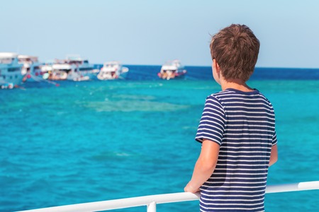 One boy in a stripy marine tshirt enjoying a boat sea trip and beautiful waters at coral reef. Travel exotic destination and family vacation concept with copy spaceの写真素材