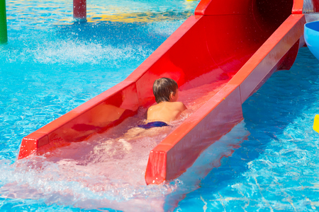 Happy cheerful boy having fun on water slide at aqua park. Summer recreation and family vacation conceptの写真素材