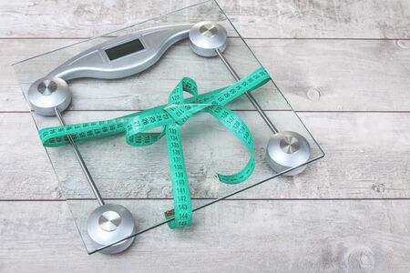 Green tape measure bow around glass weighing scale on a grey rustic surface. Healthy weight...