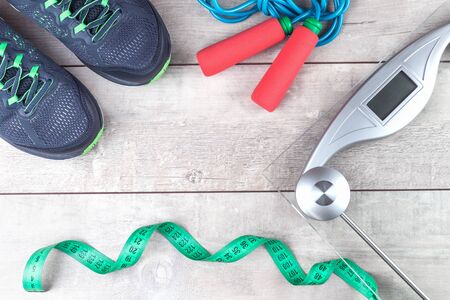 Green measure tape, glass weighing scale, jumping rope and a pair of running shoes on a rustic...