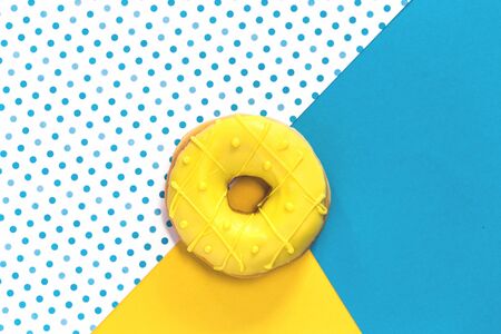 One tasty fresh Donut with yellow glaze on matching yellow and blue background. Top view flat lay with copy spaceの写真素材